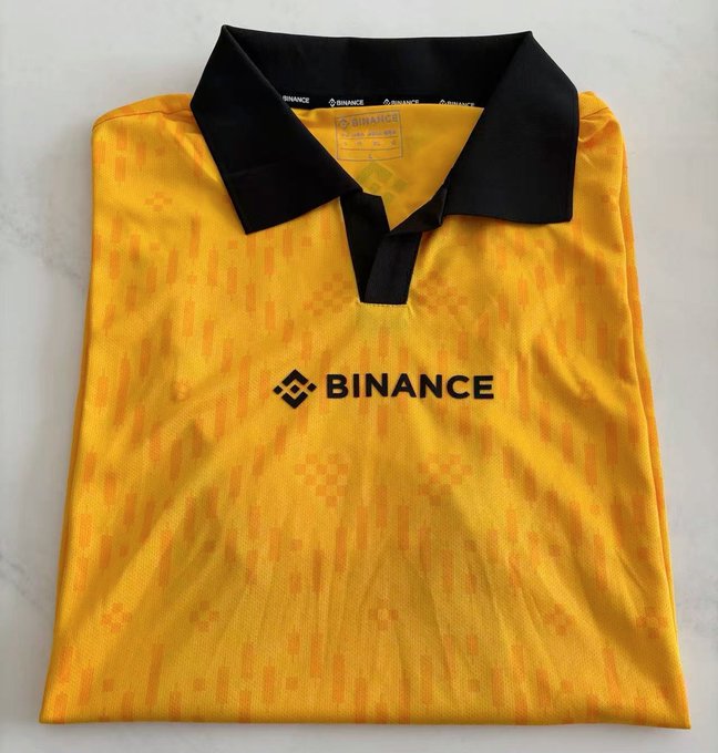 The image features a yellow shirt with black text, which reads "binance" written in white letters. The shirt appears to be folded or rolled up, possibly for storage or transportation purposes. The background of the image is white, providing contrast that makes the black text on the shirt stand out.