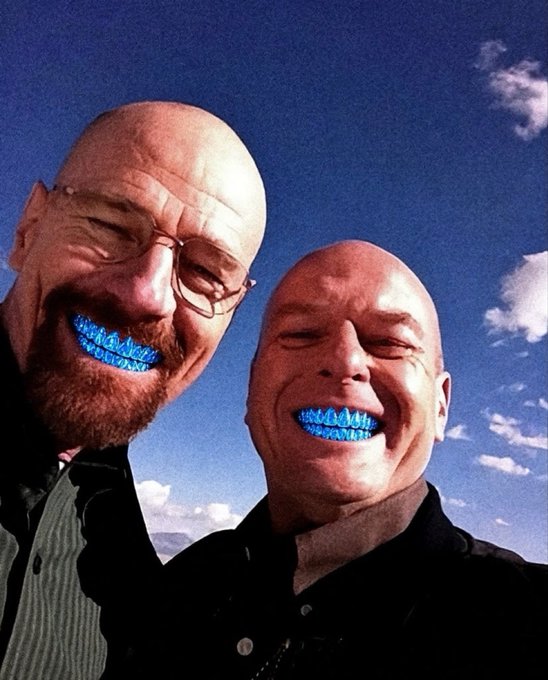 A selfie of two bald, bearded men (Walter White and Jesse Pinkman from Breaking Bad) against a blue sky, edited so their teeth glow bright blue.