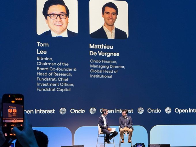 A conference stage screen displays speakers 'Tom Lee' (Bitmine, Chairman of the Board, Co-founder & Head of Research, Fundstrat) and 'Matthieu De Vergnes' (Ondo Finance, Managing Director, Global Head of Institutional) with logos for 'Open Interest' and 'Ondo' at the bottom.