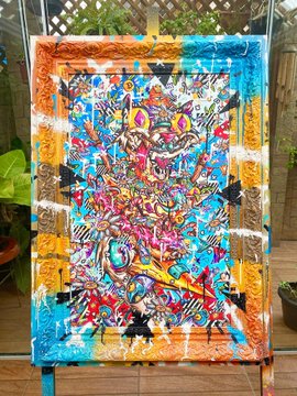 A vibrant, chaotic mixed-media painting filled with bright colors, abstract shapes, and graffiti-style markings hangs on a wooden fence outdoors.