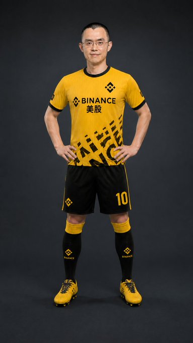 The image features a man wearing a yellow soccer uniform with black stripes and numbers standing against a black background. The text "Binance Has It All" is visible in the image, which suggests that Binance offers various services beyond just coin buying. The player's signature move, which is transformed into a feature of Binance, represents the US stocks aspect of the post.