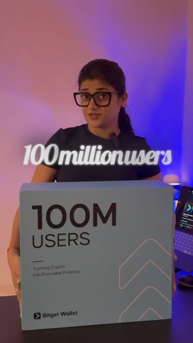 A woman in glasses holds a sign reading '100M USERS - Turning Crypto into Everyday Finance' with a Bitget Wallet logo, with overlaid text '100millionusers'.