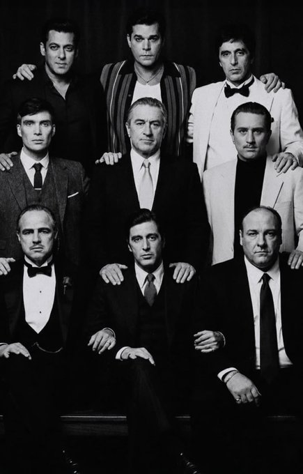 A black-and-white photograph of a posed group of nine men in suits, recognizable as a still from the movie showing Don Vito Corleone (Marlon Brando) seated at the center.