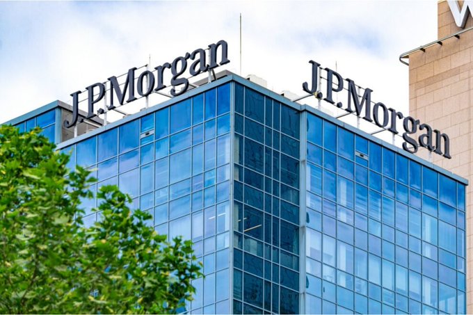 A modern glass office building displays prominent "J.P.Morgan" signage on its rooftop against a partly cloudy sky.