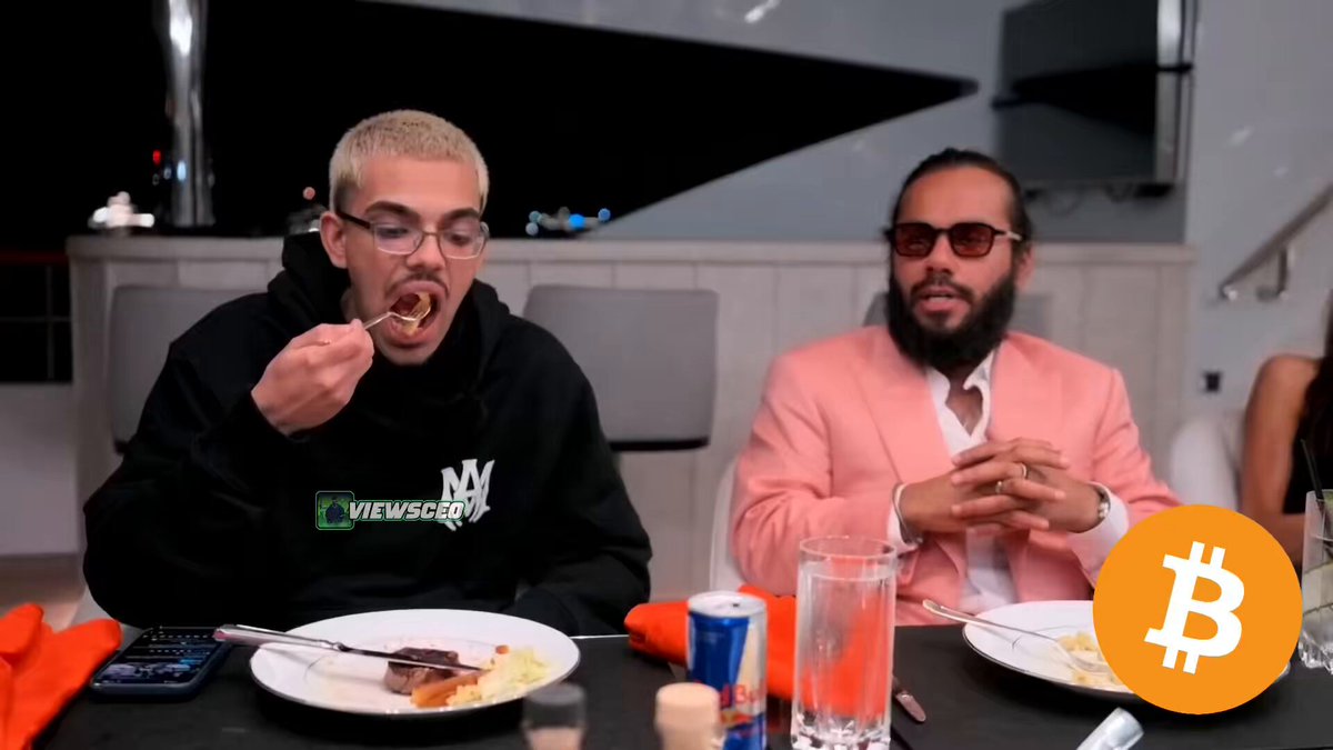 The image shows two men sitting at a table, eating food while wearing sunglasses. They are surrounded by various objects such as cups, forks, knives, and spoons. The background features a dining table with chairs around it, suggesting that they might be in a restaurant or a similar setting. A post on social media is visible, discussing the reasons behind Bitcoin's recent crash. The image includes text that reads "Monaco Billionaire reveals the SECRET behind why Bitcoin is crashing", which seems to be related to the post about Bitcoin.