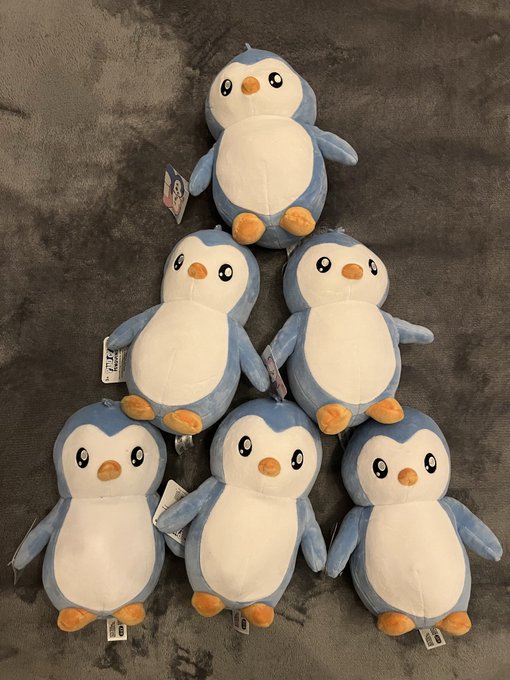 Six identical plush penguin toys with blue backs, white bellies, and orange beaks and feet are arranged in a pyramid formation on a dark gray carpet.