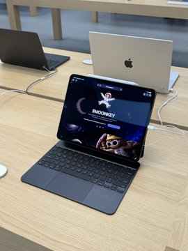 The image shows a row of Apple devices on display, with a MacBook in the foreground displaying a website or app featuring "$MOONKEY" with a monkey graphic. This aligns with the caption suggesting a playful joke about loading all the computers at the Apple Store with $MOONKEY.