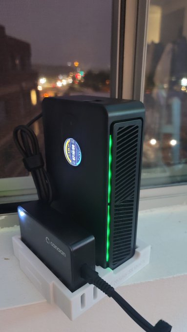 A black Spacetech electronic device with green LED lights sits on a windowsill at night, plugged into a power source.