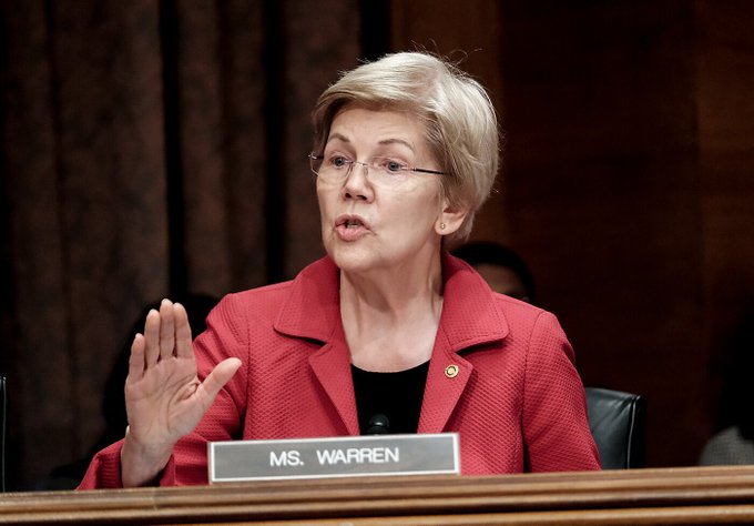 Senator Elizabeth Warren, seated at a dais with a "MS. WARREN" nameplate, gestures while speaking in opposition to the Senate's CLARITY Act, arguing the legislation contains significant gaps regarding presidential crypto financial conflicts and vulnerabilities to bad actors.