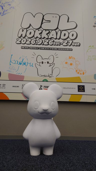 A white bear figurine sits in front of a poster for 'NEO HOKKAIDO 2026' art exhibition featuring event details and illustrations.