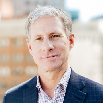 A headshot of Chris Larsen, the co-founder of Ripple, in a navy blazer and checkered shirt. The image accompanies news of his investment in American Perpetuals Exchange, a derivatives platform co-founded by Senator Kirsten Gillibrand's son.