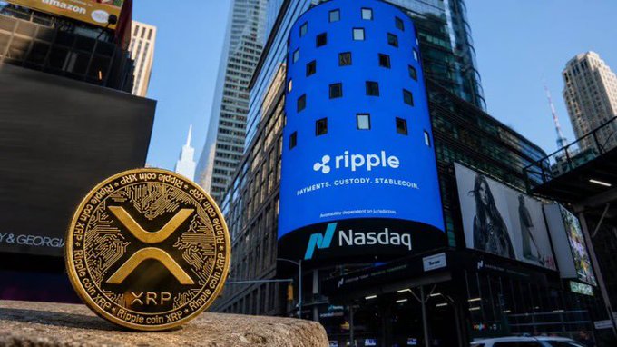 A gold XRP/Ripple coin sits in the foreground while a large blue billboard displaying the Ripple logo and the text 'PAYMENTS. CUSTODY. STABLECOIN' towers above the Nasdaq building in the background.