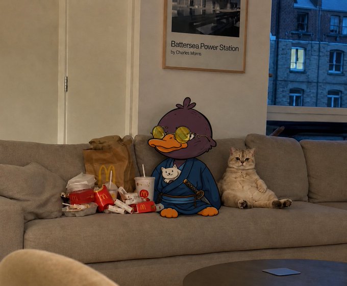 The image features two cartoon ducks sitting on a couch, surrounded by various food items such as sandwiches and drinks. The scene appears to be set up for a photo shoot or an artistic project that involves the ducks as characters within a room with a dining table nearby. The focus of the image is on the ducks' presence in this setting, capturing their unique personalities amidst everyday objects like sandwiches and drinks.