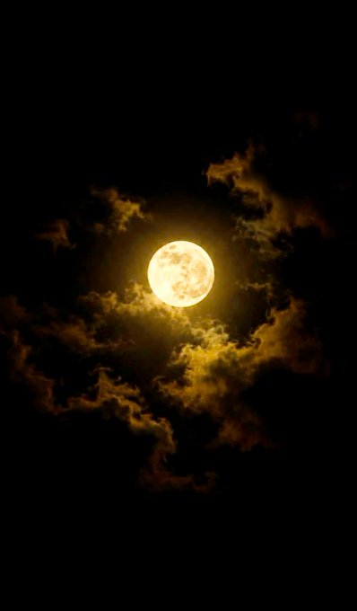 A full moon glows golden through scattered clouds in a dark night sky.