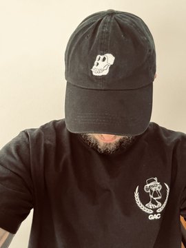 A person wearing a black cap with a small white skull logo, obscuring their face, and a black t-shirt with a white skull and 'GMC' graphic.
