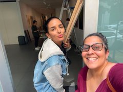 Two women smiling for a selfie, one with dark hair and a denim jacket, and the other wearing glasses and a maroon top.