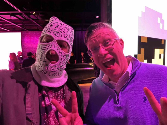 Beeple (in his signature scribbled white balaclava) poses with a grinning fan flashing peace signs, both bathed in pink/magenta light at an event, visually confirming the post's "Can you see this?" GM moment as they hype his algorithm and the @toadswiback collab.