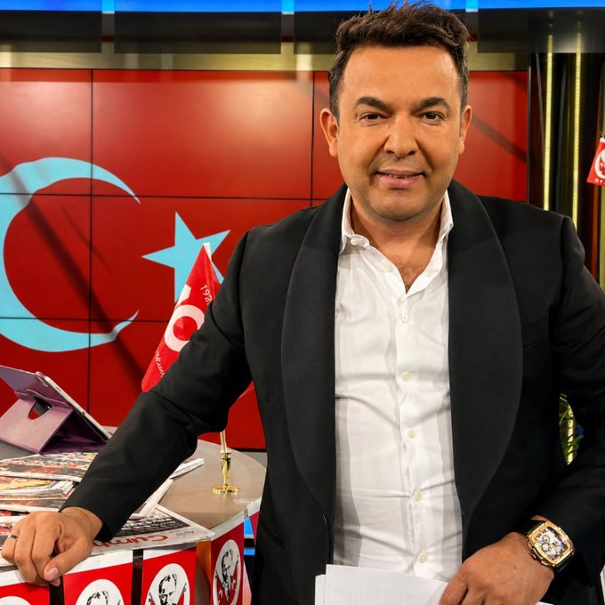 A man in a black blazer and white shirt smiles at the camera in a TV studio featuring red backdrop panels with the Turkish crescent and star emblem, alongside a small Turkish flag. The post references a report by Burak Doğan about Tahir Sarıkaya's crypto account showing 27 million 573 thousand TL in detected outflows, suggesting the man pictured may be the journalist or subject of this financial news segment.