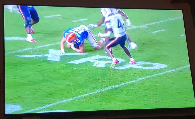 A TV broadcast shows a college football player on the ground near yard markers, with the ticker "XRP" prominently painted on the field, capturing the XRP advertising being promoted in the post.