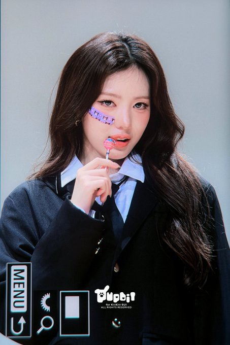 A young woman with long dark hair and a black blazer holds a lollipop, with a 'MENU' overlay and the 'tripleS' logo visible.