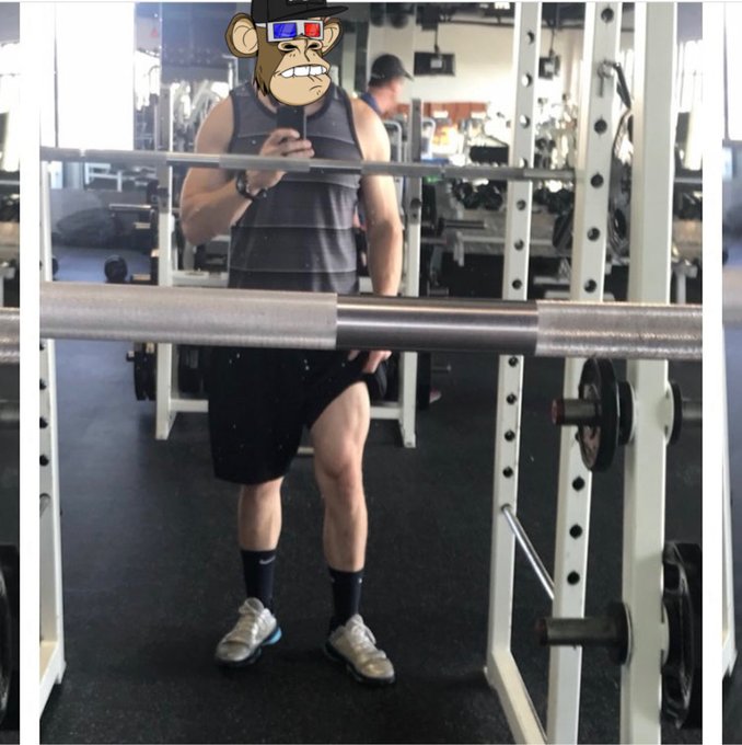 A gym-goer poses for a mirror selfie holding a smartphone, wearing a striped tank top, black shorts, black socks, and sneakers while holding a barbell across a squat rack. Their face has been digitally replaced with a cartoon monkey wearing 3D glasses.