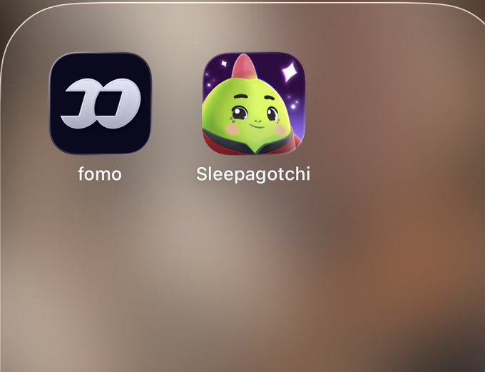 Two app icons are displayed on a blurred background: a dark icon labeled "fomo" and a green character icon with a pink bow labeled "Sleepagotchi".