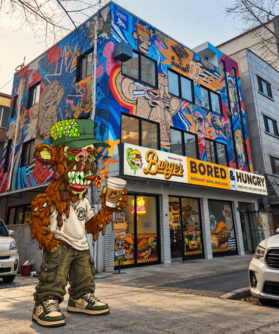 A vibrant street view of 'Bored & Hungry' American-style burger restaurant with colorful murals on the building facade, featuring a cartoon zombie character holding a coffee cup and burger in the foreground.