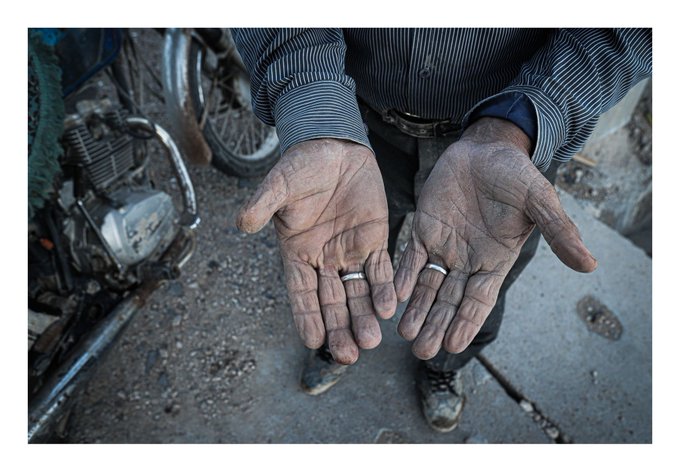 A mechanic shows his dirt-covered hands, wearing a silver ring, with a motorcycle engine visible in the background.