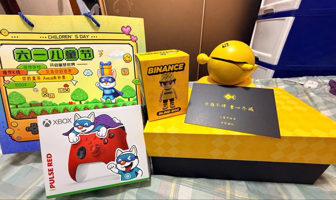 The image features a collection of items, including a Nintendo Wii game system, a yellow ball, and some books. The Nintendo Wii game system appears to be a gift from Binance, while the yellow ball could possibly be a gift from another company or an item for personal use. The books are scattered around the scene, adding variety to the objects present in the image.