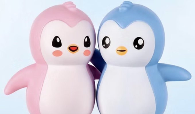 Two cute penguin-like figurines, one pink and one blue, standing side by side with large shiny eyes and orange beaks against a light background.