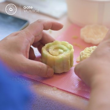A promotional image for "GATEVOYAGE" showing hands shaping a green matcha mooncake on a pink silicone mat, with a cup of tea and another mooncake visible in the background.