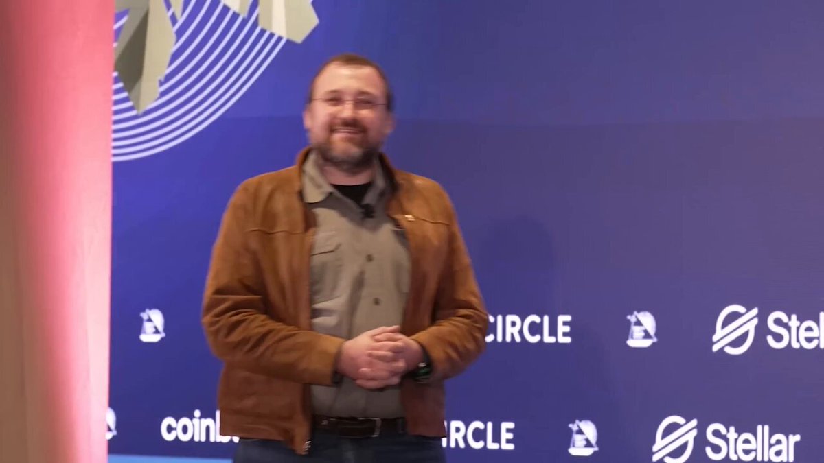 The image features a man standing in front of a blue wall with white text, which reads "circle" and "Starlar". The man appears to be smiling as he poses for the photo. In the background, there are logos for companies such as "Coin" and "ADA", indicating that this is likely an event related to cryptocurrency or digital assets.