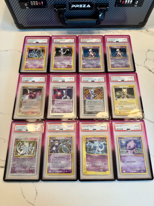 Twelve graded Pokémon trading cards, including Mewtwo and Mew, are displayed in protective slabs on a marble surface in front of a Preza briefcase.