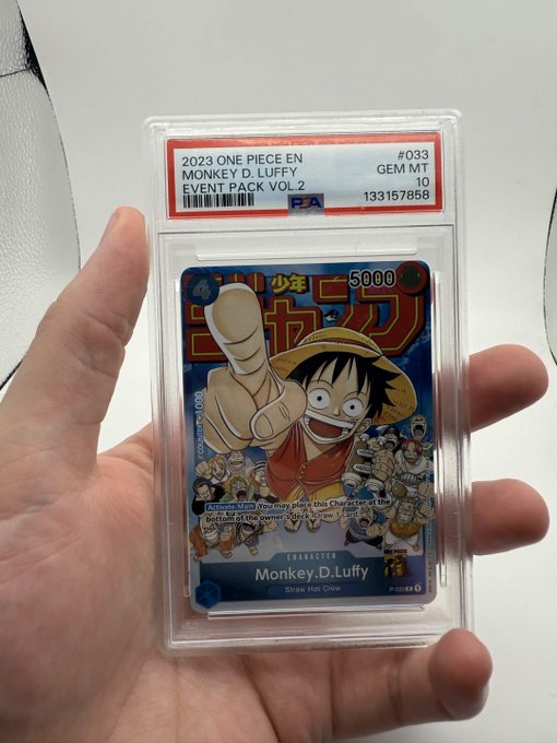 A hand holding a PSA-graded 10 GEM MT One Piece trading card, card #033 featuring Monkey D. Luffy (Straw Hat Crew) from the 2023 Event Pack Vol. 2.