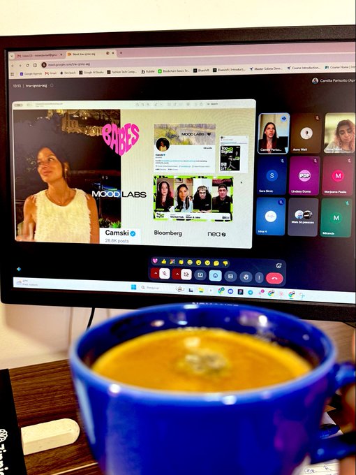 A computer monitor displays a Google Meet call with multiple participants, while a blue mug filled with coffee sits on the desk in the foreground.