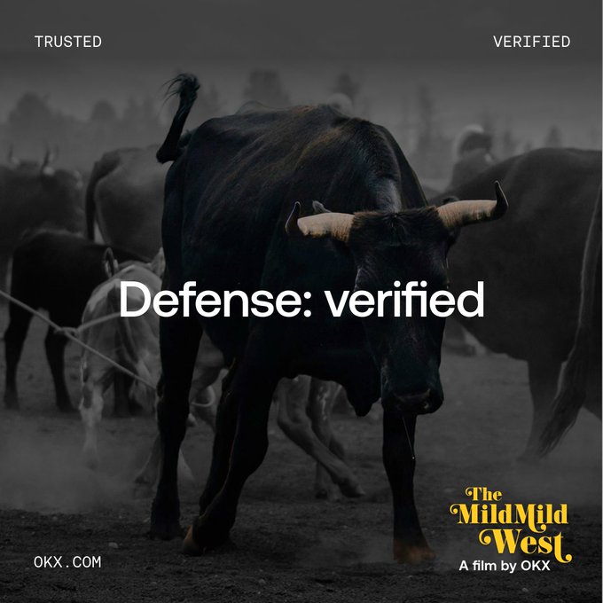 A dark, dramatic image shows a powerful bull charging forward through dust, surrounded by a herd of cattle, with the text "Defense: verified" overlaid in the center and "TRUSTED" and "VERIFIED" in the top corners. The "OKX.COM" branding and "The Mild Mild West - A film by OKX" logo appear at the bottom, reinforcing the ad's message of OKX as a trustworthy, verified crypto platform amid the "chaos" of the crypto frontier.