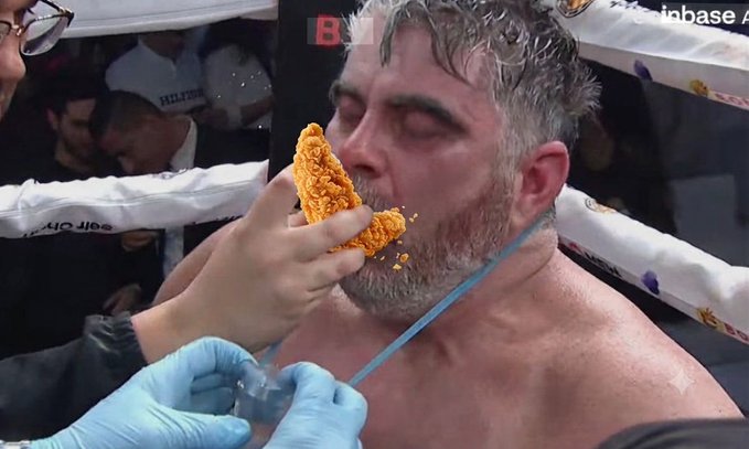 A boxer with a gray beard eats a piece of fried chicken in the ring while a person wearing blue gloves holds an oxygen mask near his face, referencing the cryptocurrency post's metaphor of "tendies" (slang for profits). Visible text includes "Coinbase," "Billions," and "eat City" in the background, tying into the post's promise of massive financial gains from the meme stock or crypto token.