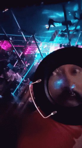 The image shows a person wearing a red shirt holding up a camera with their face visible through the lens, possibly taking a selfie or recording something interesting. The background of the photo features neon lights and a cityscape, creating an urban atmosphere. The caption on the image reads "Heads up If you've collected my Ethereum work, watch your DMs. You have a free claim in my new project. I'M REACHING OUT PRIVATE. IT'S REAL."