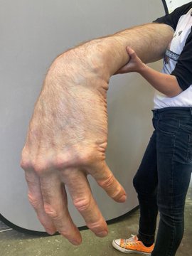 A person holds a large, highly detailed prop hand that appears to be from a costume or special effects project.