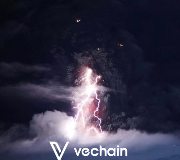 The image features a large lightning bolt striking a volcano or geyser, creating an intense display of light and heat. The caption above the image reads "THE STORM IS BUILDING... A massive lightning strike is about to hit #VeChain - the TRUST AI Marketplace is launching and ready to electrify the entire ecosystem!". This suggests that the image is related to a post on social media, possibly promoting an event or product launch. The lightning bolt serves as a visual representation of the energy and excitement associated with the launch, while also emphasizing the power and unpredictability of nature.