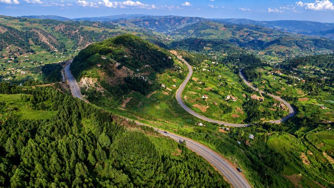 The image shows an aerial view of a winding road through a lush green valley, surrounded by trees. The road curves around the mountain side, adding a sense of adventure and excitement to the scene. Below the picturesque landscape, there are several cars driving along the winding road, indicating that it is a popular route for transportation or leisurely drives. The image also includes text elements such as "Happy Monday A new week means new opportunities onchain Keep showing up, keep learning, and keep building on Base. Stay active. Stay focused. Stay Based @base @baseapp @jessepollak @buildonbase". This suggests that the road is a significant part of the community's daily life or recreational activities in this area.
