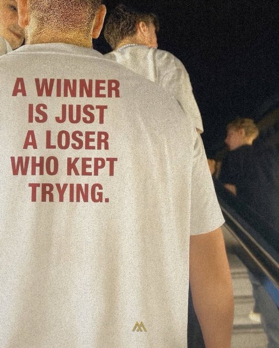 The back of a person wearing a white t-shirt with red text reading 'A WINNER IS JUST A LOSER WHO KEPT TRYING.'