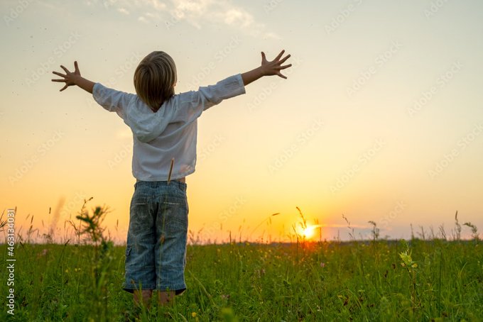 Adobe Stock image showing a child with outstretched arms standing in a grassy field at sunset, facing away from the camera toward the setting sun.