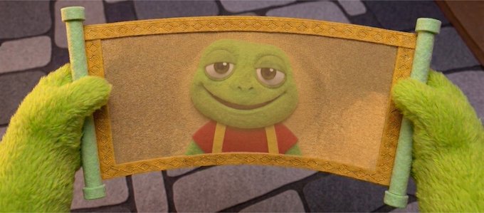A scene from Shrek showing green furry hands holding up a scroll/painting depicting a smiling frog or toad character wearing a red shirt and yellow overalls.