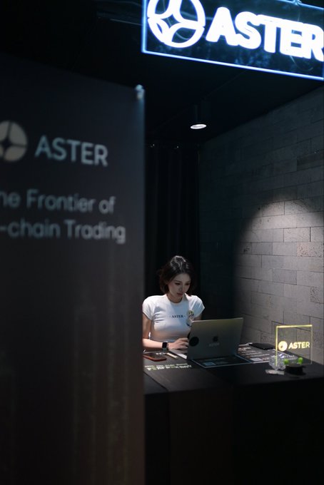 A woman in a white ASTER shirt works on a laptop at an "ASTER" branded booth advertising itself as "The Frontier of [On]-chain Trading," capturing a moment during her day at the KBW event.