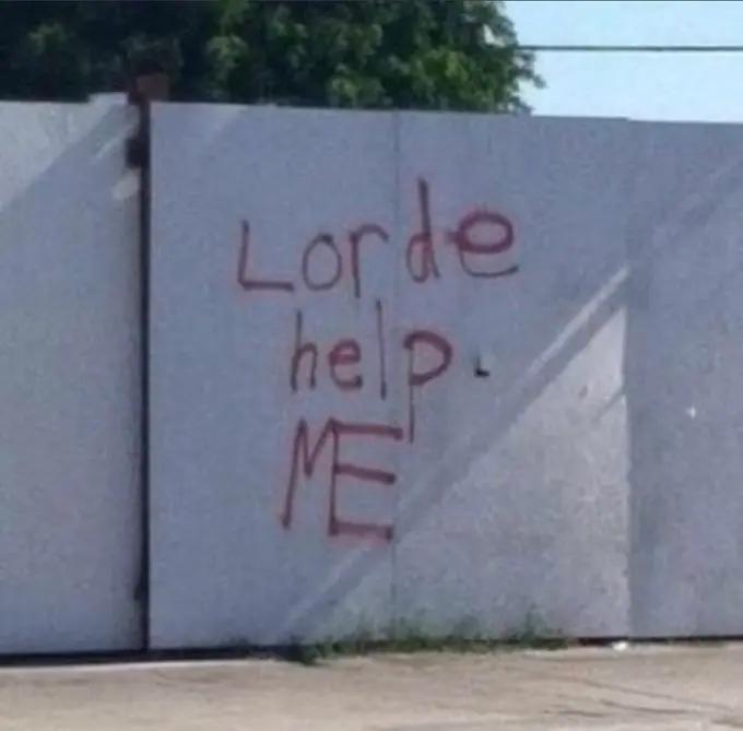 Red spray-painted graffiti on a light blue wall reads "Lorde help ME" with an arrow pointing down.