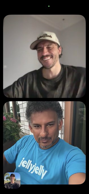 A split-screen video call shows a smiling man in a cap in the top frame and a man wearing a blue 'jellyjelly' t-shirt in the bottom frame.