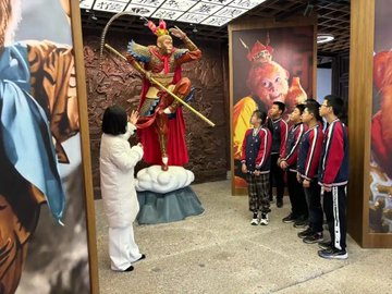 Children and an adult gather before a statue of Sun Wukong, the Monkey King, in what appears to be a museum or cultural exhibit, possibly paying respects following news of related figures' passing.