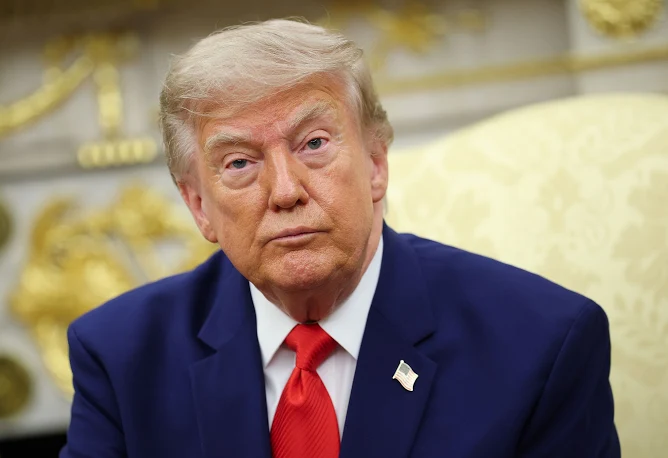 A portrait photo of Donald Trump wearing a dark blue suit and red tie in what appears to be the Oval Office.