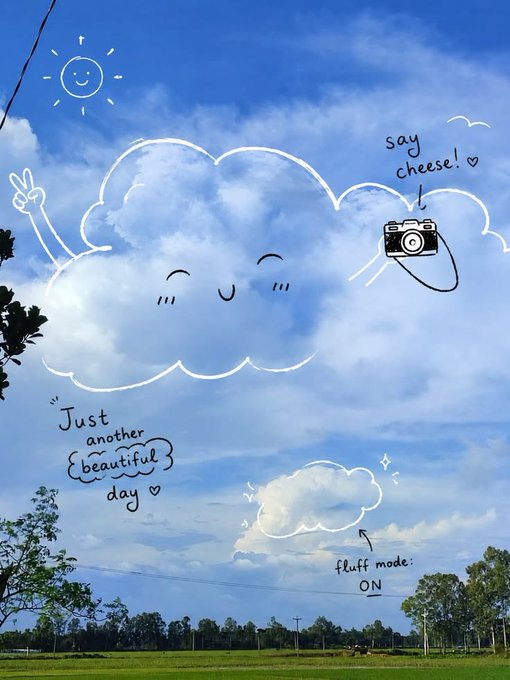A photograph of a blue sky with white clouds, decorated with digital doodles including a smiling sun, a peace sign, a camera with 'say cheese!', and the text 'Just another beautiful day' and 'fluff mode: ON'.